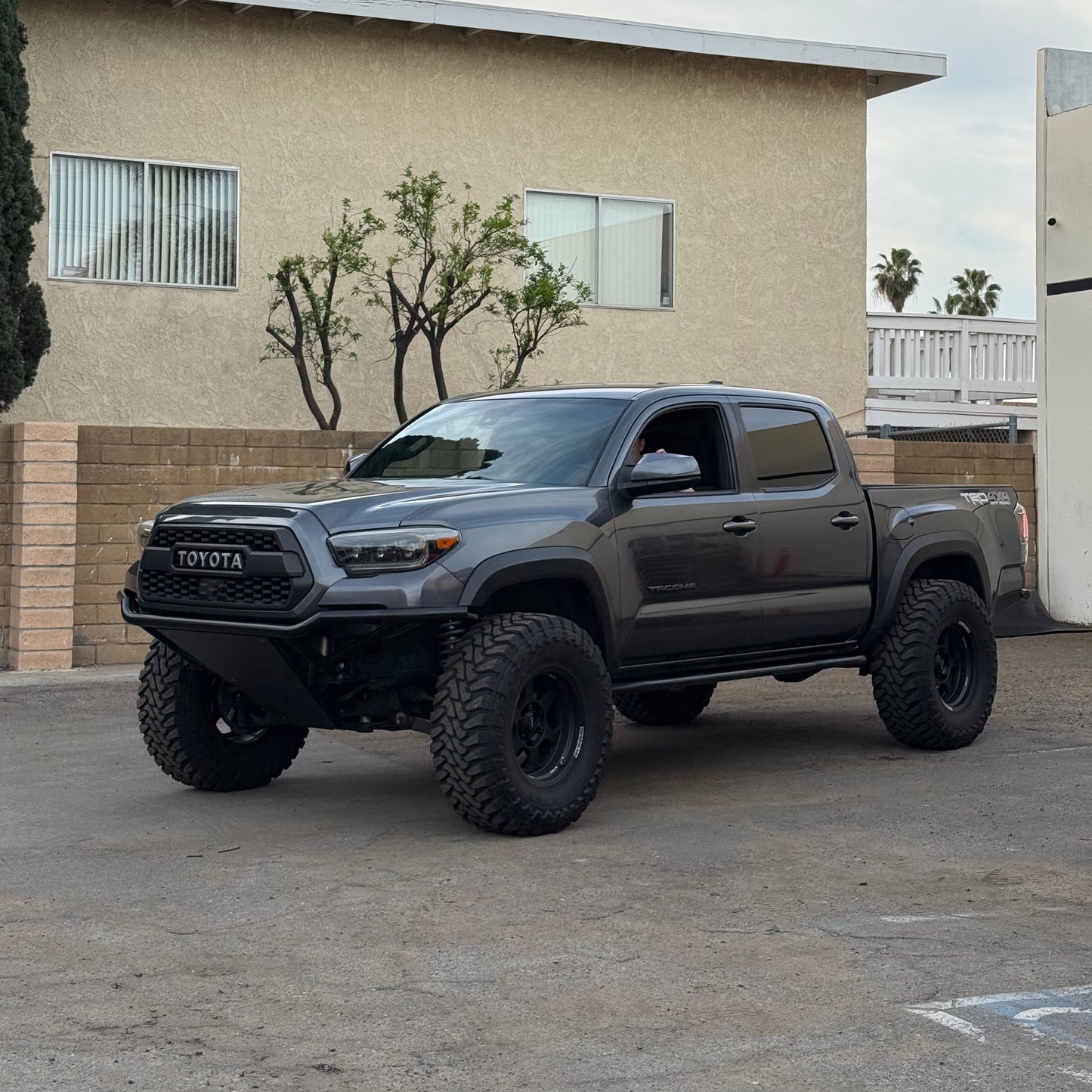 Gray Toyota truck parked in front of a beige building with a cloudy sky.